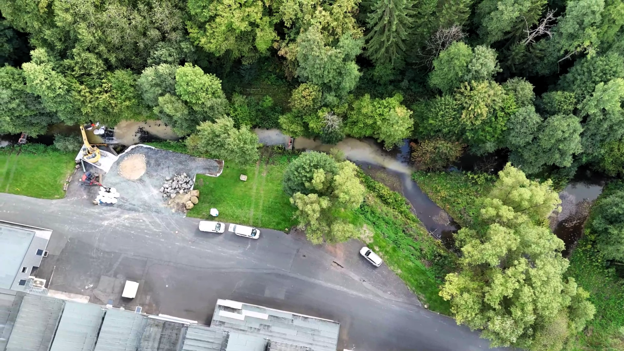 Dietzhölze – Wiederaufnahme Baumaßnahme 2026 Header Luftaufnahme von einem Wald mit einem kleinen Fluss und Baufahrzeugen